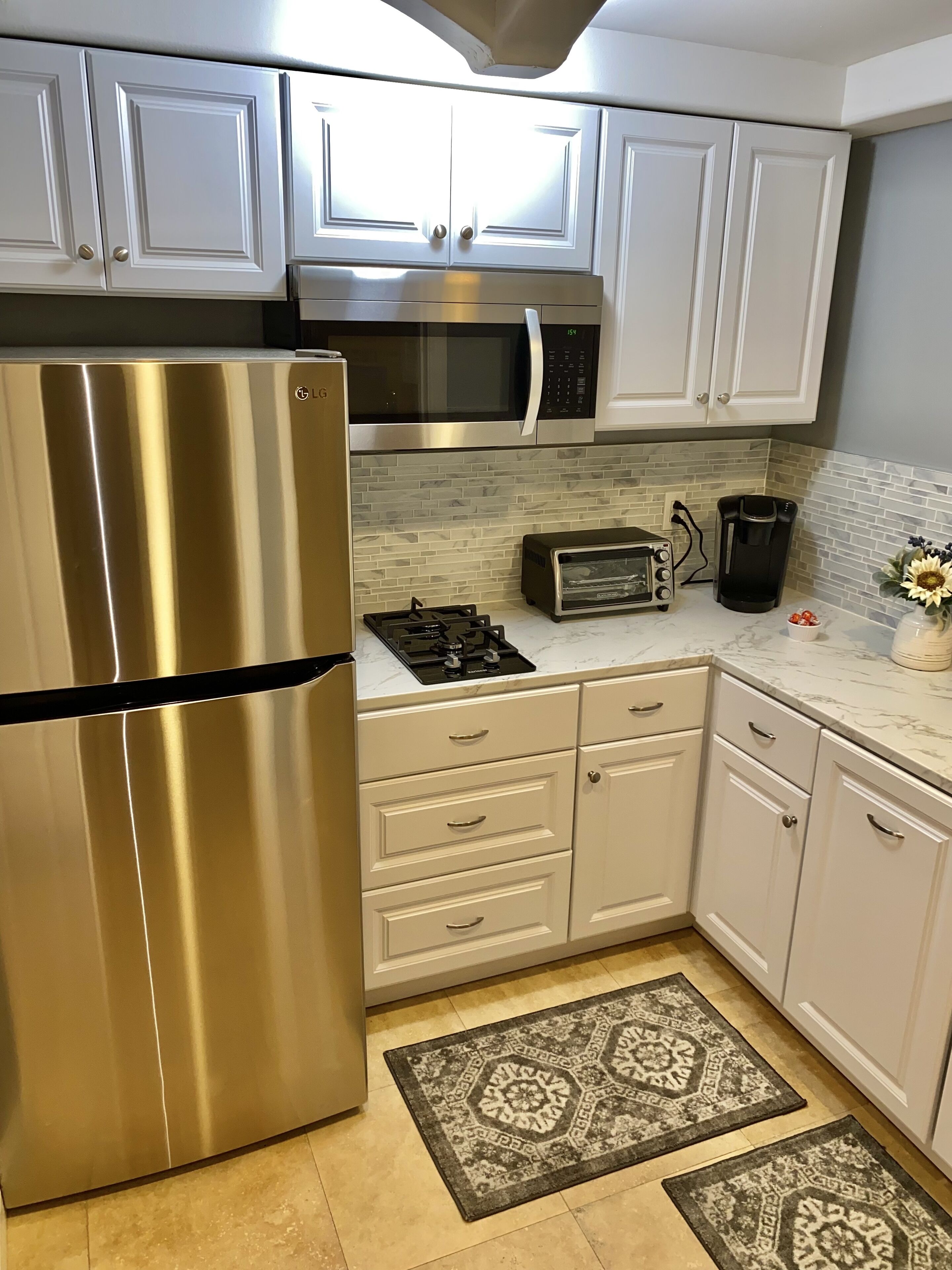 A kitchen with white cabinets, stainless steel appliances, a microwave, a toaster, and a coffee maker.