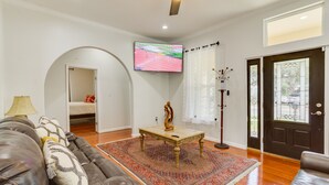 Un salon avec un canapé en cuir, une table basse, un téléviseur fixé au mur, un tapis à motifs et une porte avec un panneau en verre.