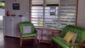 Une pièce comprenant deux fauteuils verts à motifs floraux, une petite table en bois et un meuble blanc.