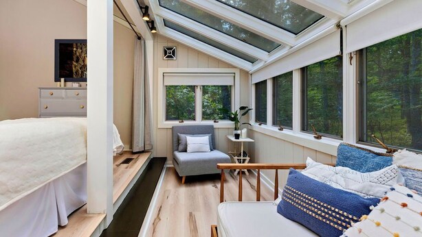 Une chambre avec un puits de lumière, un lit, une chaise, une table de chevet et une vue sur les arbres.