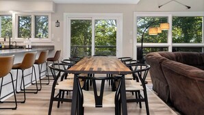 Un espace repas moderne avec une table et des chaises en bois, un coin bar et une grande fenêtre donnant sur la forêt.