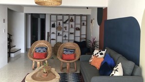A modern living room with a grey sofa, two wicker chairs, a woven pendant light, and a wooden coffee table. - Matatlán, Casa Crónica (Oaxaca de Juárez)