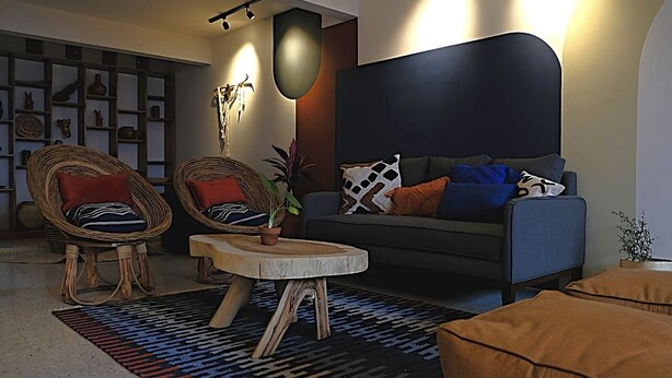 A modern living room with a dark grey sofa, two wicker chairs, a wooden coffee table, and a patterned rug. - Matatlán, Casa Crónica (Oaxaca de Juárez)