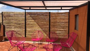 A covered outdoor seating area with metal chairs and a table, a bamboo fence, and a clear blue sky. - Matatlán, Casa Crónica (Oaxaca de Juárez)