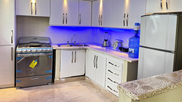 A modern kitchen with white cabinets, a stove, a sink, a blender, and a refrigerator. - RA-4 cómodo apartamento con vista al mar (Samaná)