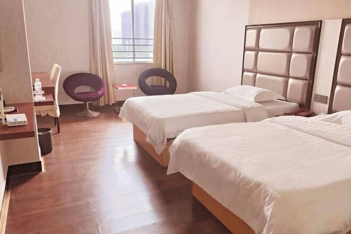 Une chambre d’hôtel avec deux lits, un bureau avec une chaise, une fenêtre avec des rideaux et une vue sur les immeubles.
