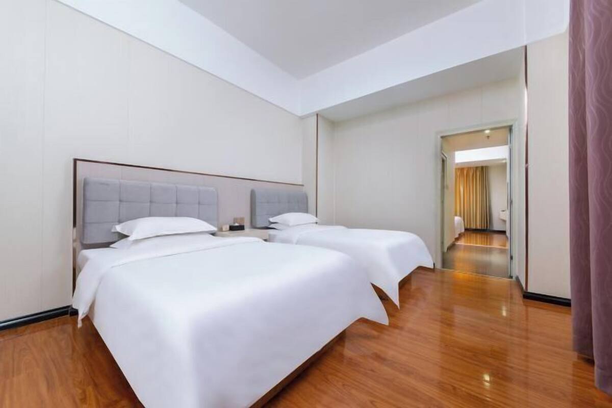 Une chambre d’hôtel avec deux lits, un plancher en bois et un couloir menant à une autre pièce.