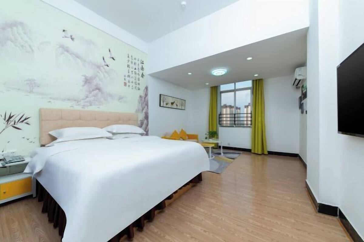 Une chambre d’hôtel moderne dotée d’un grand lit, d’un bureau, d’une chaise, d’une fenêtre avec des rideaux et d’un mur orné d’œuvres d’art.