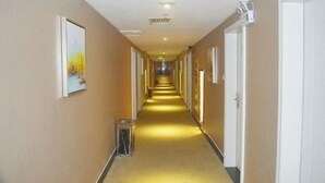 A long, narrow hotel corridor with doors on both sides, a trash bin in the center, and a painting on the left wall. - Senlian City Express Hotel (Qingyuan Gulongxia City Beiqi Station Store) (Qingyuan)