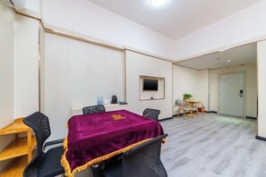 Une salle de conférence avec une table recouverte d’une nappe violette, des chaises noires, une petite table d’appoint en bois, un téléviseur fixé au mur et une porte à l’arrière-plan.