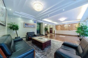 A hotel lobby with leather sofas, a coffee table, a reception desk, and a chandelier.