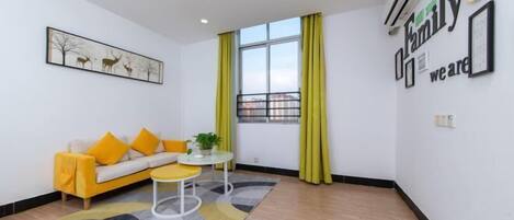 Una sala de estar moderna con un sofá amarillo, una mesita redonda y un amplio ventanal con cortinas amarillas.
