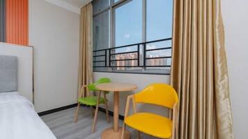 Une chambre d’hôtel avec un lit, une fenêtre donnant sur des immeubles, une petite table ronde, deux chaises et des rideaux.