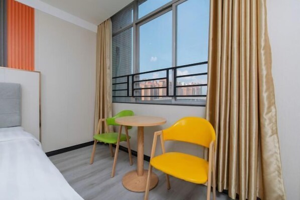 Une chambre d’hôtel avec un lit, une fenêtre donnant sur des immeubles, une petite table ronde, deux chaises et des rideaux.