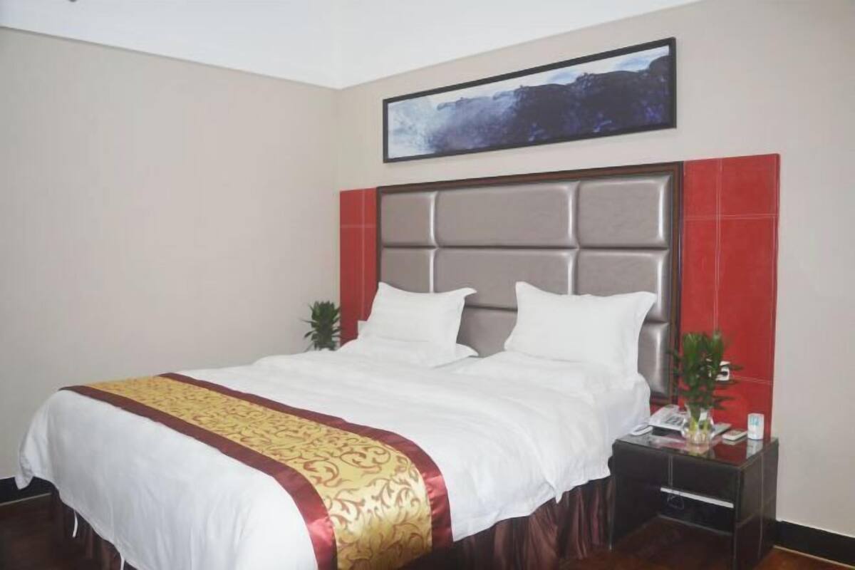 Une chambre d’hôtel avec un grand lit, une tête de lit, une table de chevet, un téléphone et un tableau encadré au mur.