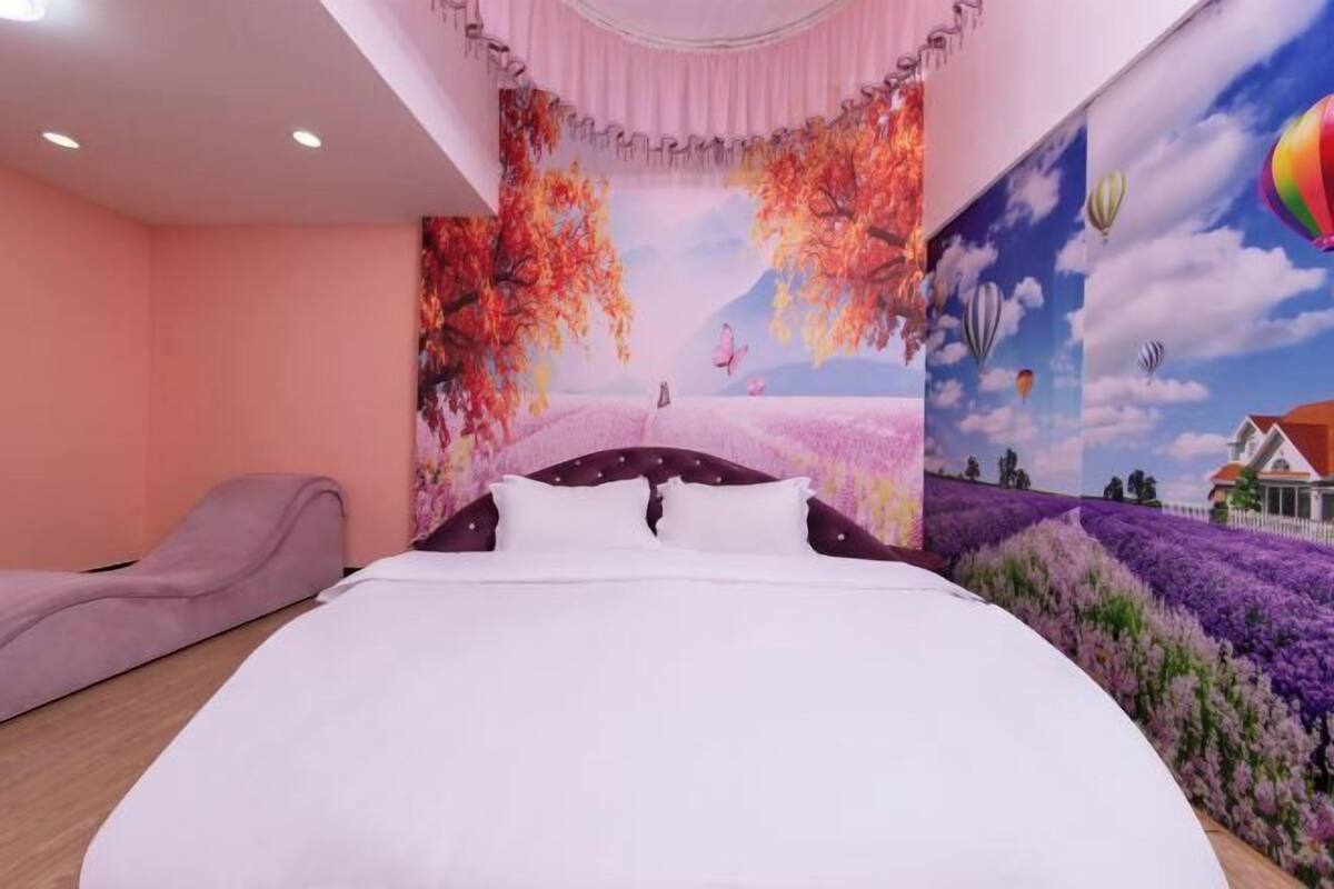 Une chambre à coucher avec un grand lit, un mur rose et une fresque représentant des arbres et des montgolfières.