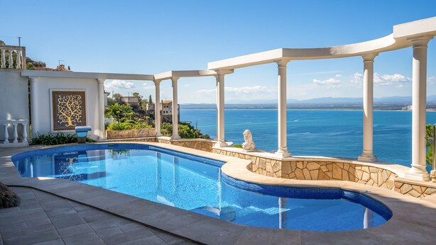 Una piscina con vistas al mar, rodeada de columnas blancas y muros de piedra.