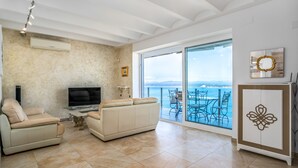 Un salón con sofá, televisor y balcón con mobiliario exterior.