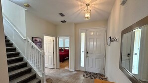 Um corredor com escada, porta de acesso a um quarto e área de jantar com mesa.