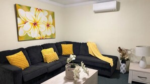 A living room with a black sofa, yellow cushions, a white coffee table, and a large floral painting on the wall.