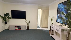 A living room with a flat-screen TV, a light-colored console table, a large potted plant, and a door leading to another room.