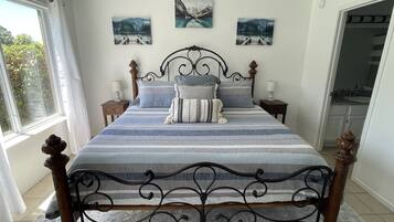 Ein Schlafzimmer mit einem Bett, zwei Nachttischen, einem Deckenventilator und drei Landschaftsbildern an der Wand.