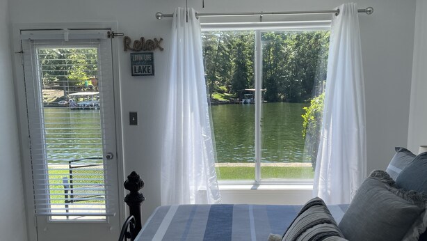 Un dormitorio con un ventanal grande que da a un lago, una cama con ropa de cama a rayas y vistas de barcas en el agua.