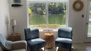Una sala de estar con dos sillones, una lámpara, una mesita redonda y vistas a un lago a través de un ventanal.