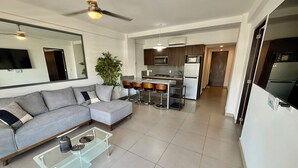 Una sala moderna con un sofá seccional gris, una mesa de centro de vidrio y una zona de cocina con un comedor.