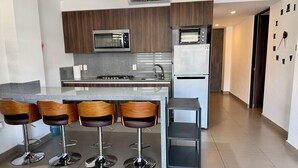 Una cocina moderna con una isla central, taburetes de bar, microondas, horno empotrado y refrigerador.