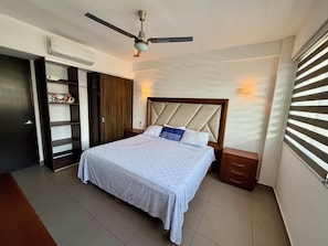 Une chambre à coucher comprenant un lit, un ventilateur de plafond, une armoire et une fenêtre avec des stores.