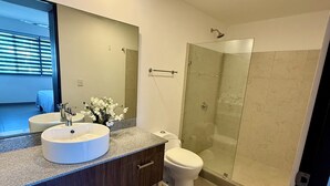 Un baño moderno con un espejo grande, dos lavamanos, un inodoro y una ducha con cerramiento de vidrio.