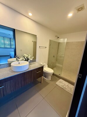 Une salle de bain moderne avec un grand miroir, deux lavabos, des toilettes et une douche à parois de verre.