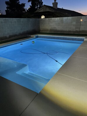 Una piscina con línea de agua cristalina, rodeada por un pavimento de hormigón y un muro bajo.
