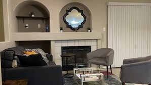 Una sala de estar con ventilador de techo, chimenea, dos sofás, una mesa de centro y un tapete estampado.