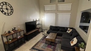 Una sala de estar con sofá, mesa de centro, televisor y estanterías.
