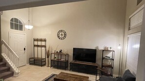 Una sala de estar con sofá, televisor, mesa de centro y una escalera que lleva a una puerta.