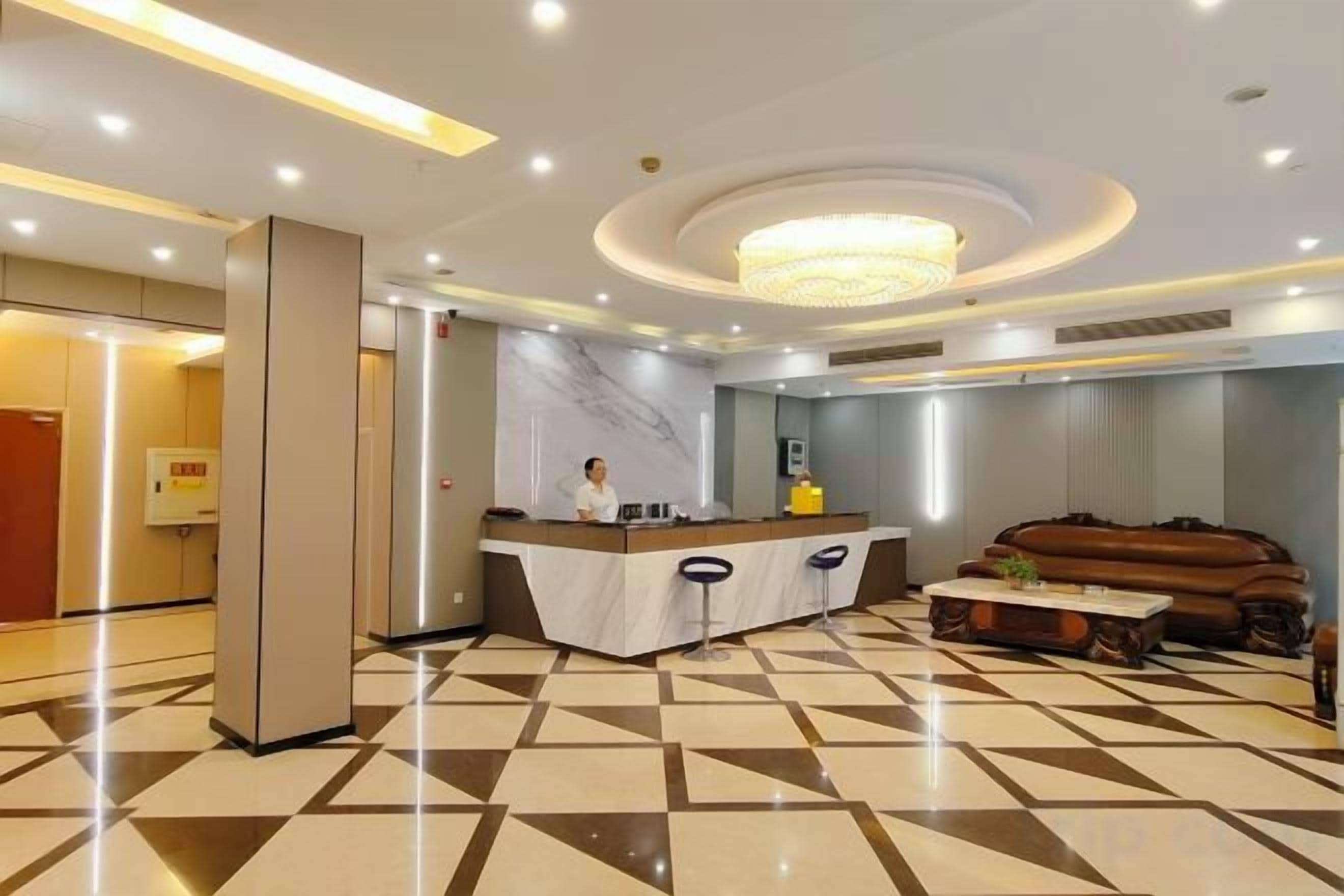 A hotel lobby with a reception desk, a large chandelier, and a patterned floor.