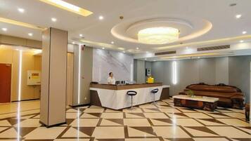 A hotel lobby with a reception desk, a large chandelier, and a patterned floor.