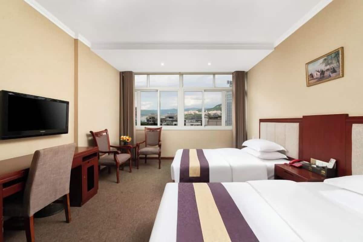 A hotel room with two beds, a TV, a desk, and a chair.