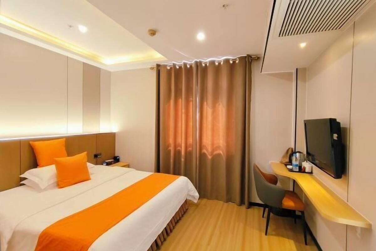 A hotel room with a bed, a desk with a TV, and a curtain.