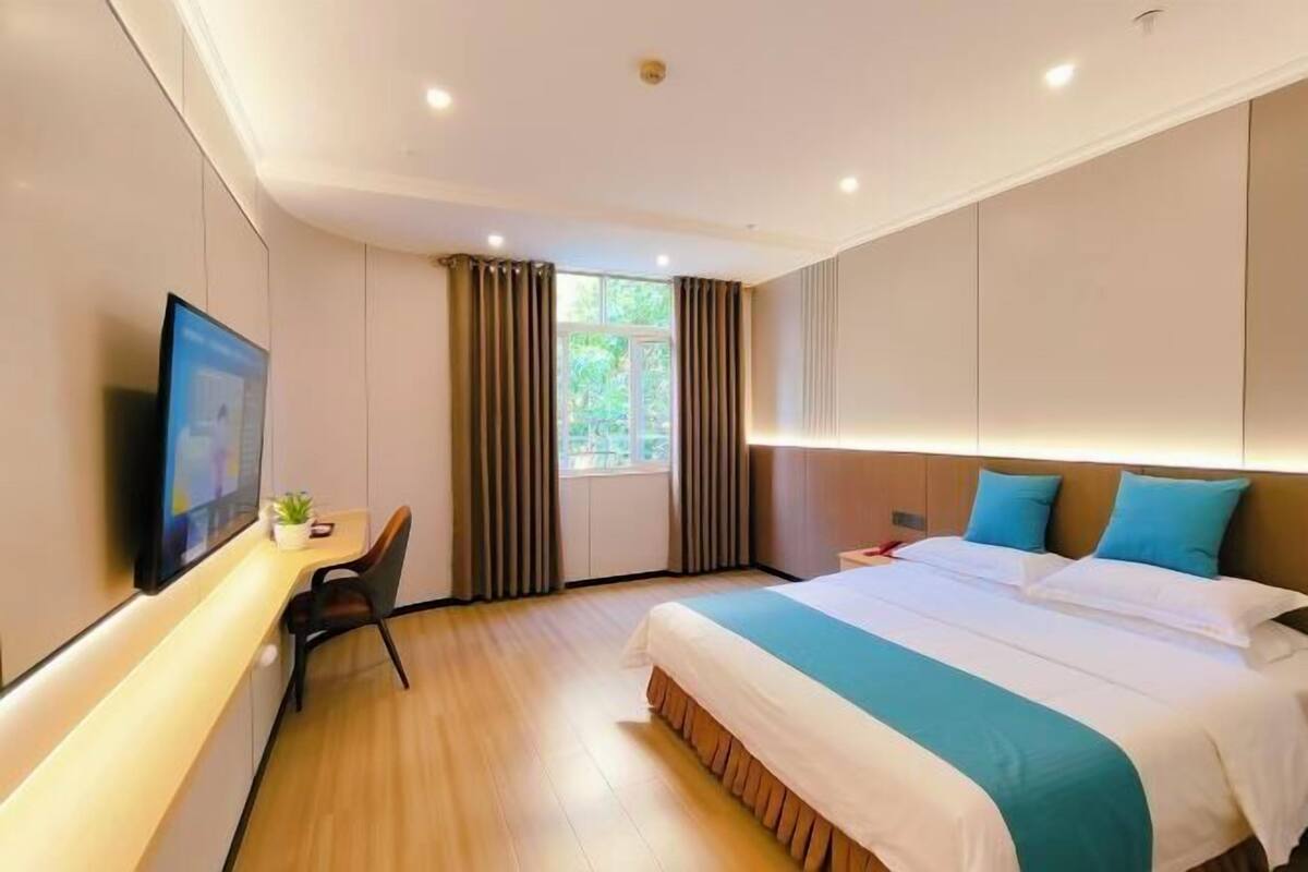 A hotel room with a bed, a desk, a chair, a TV, and a window with curtains.
