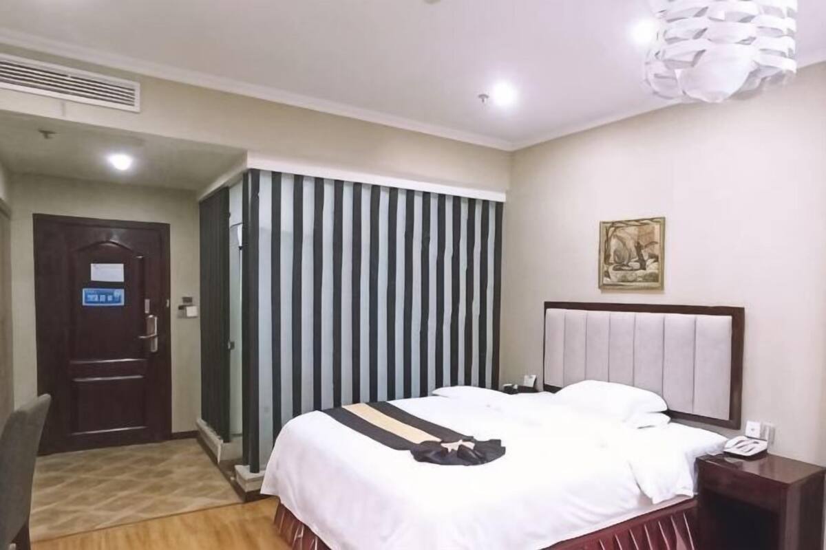 A hotel room with a bed, a bedside table, a chair, a door, and a striped curtain.