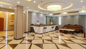 Um hall de hotel com uma mesa de recepção, um lustre grande, um chão estampado e um sofá de couro.