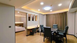 Quarto de hotel com cama, escrivaninha com cadeira, mesa de jantar com cadeiras e um espelho grande.