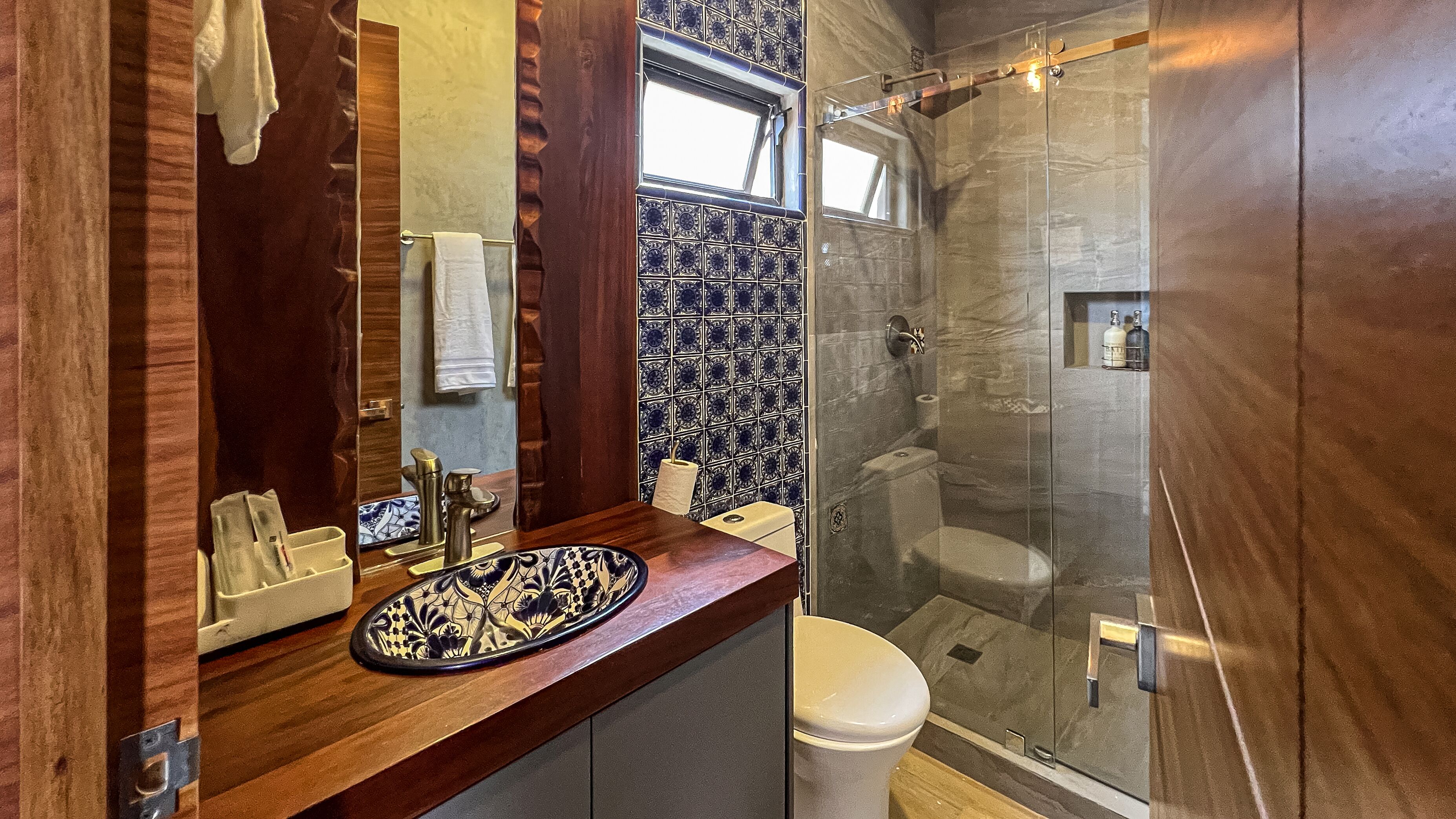 A modern bathroom with a wooden vanity, a glass shower enclosure, and a decorative tile backsplash.