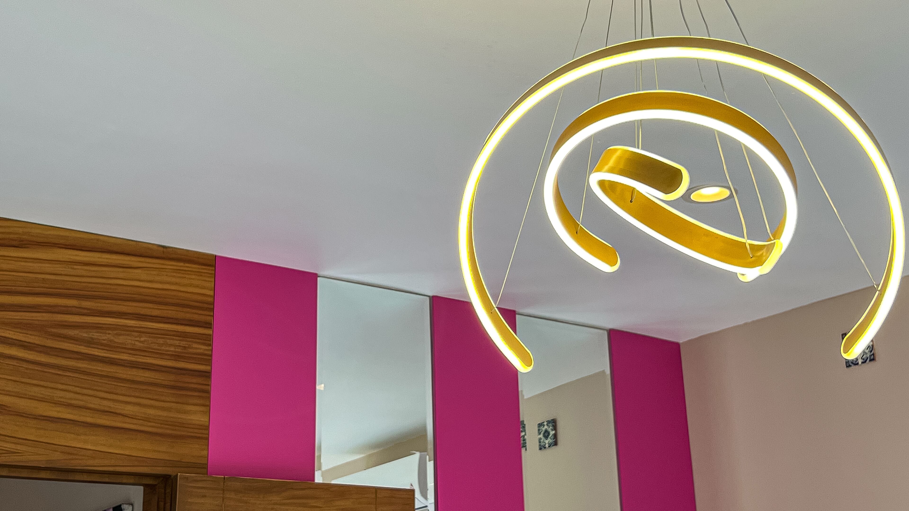 Un interno moderno caratterizzato da un lampadario curvo originale e pareti di un vivace color rosa.