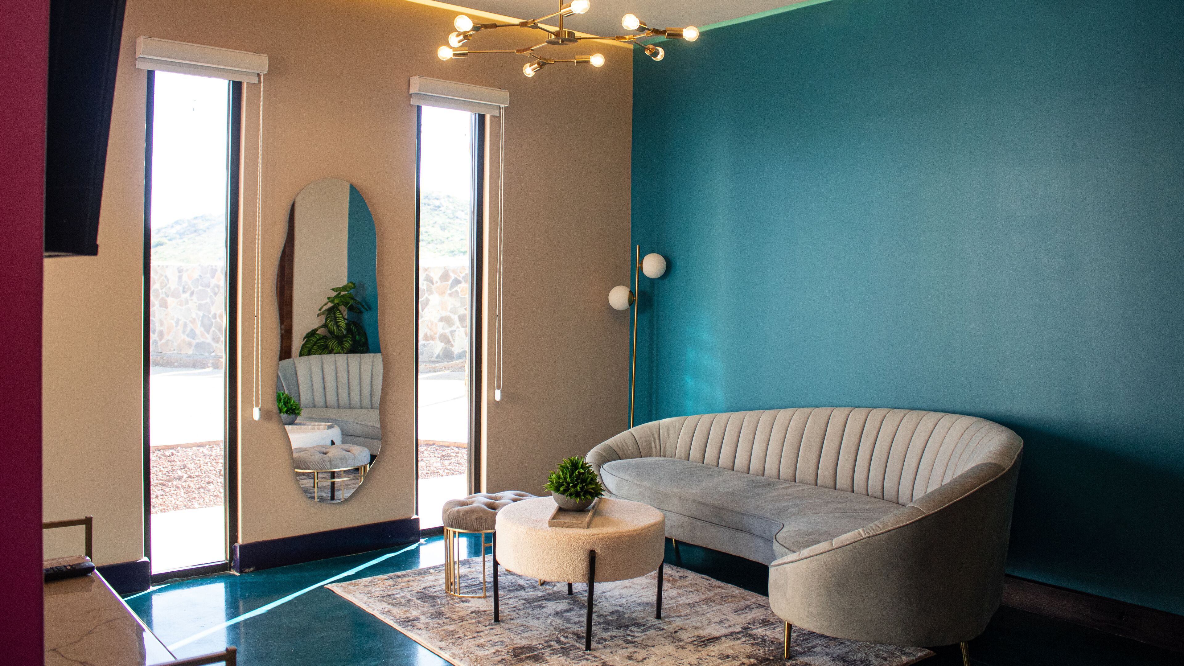 A modern living room with a curved sofa, a round ottoman, a mirror, and a floor lamp.