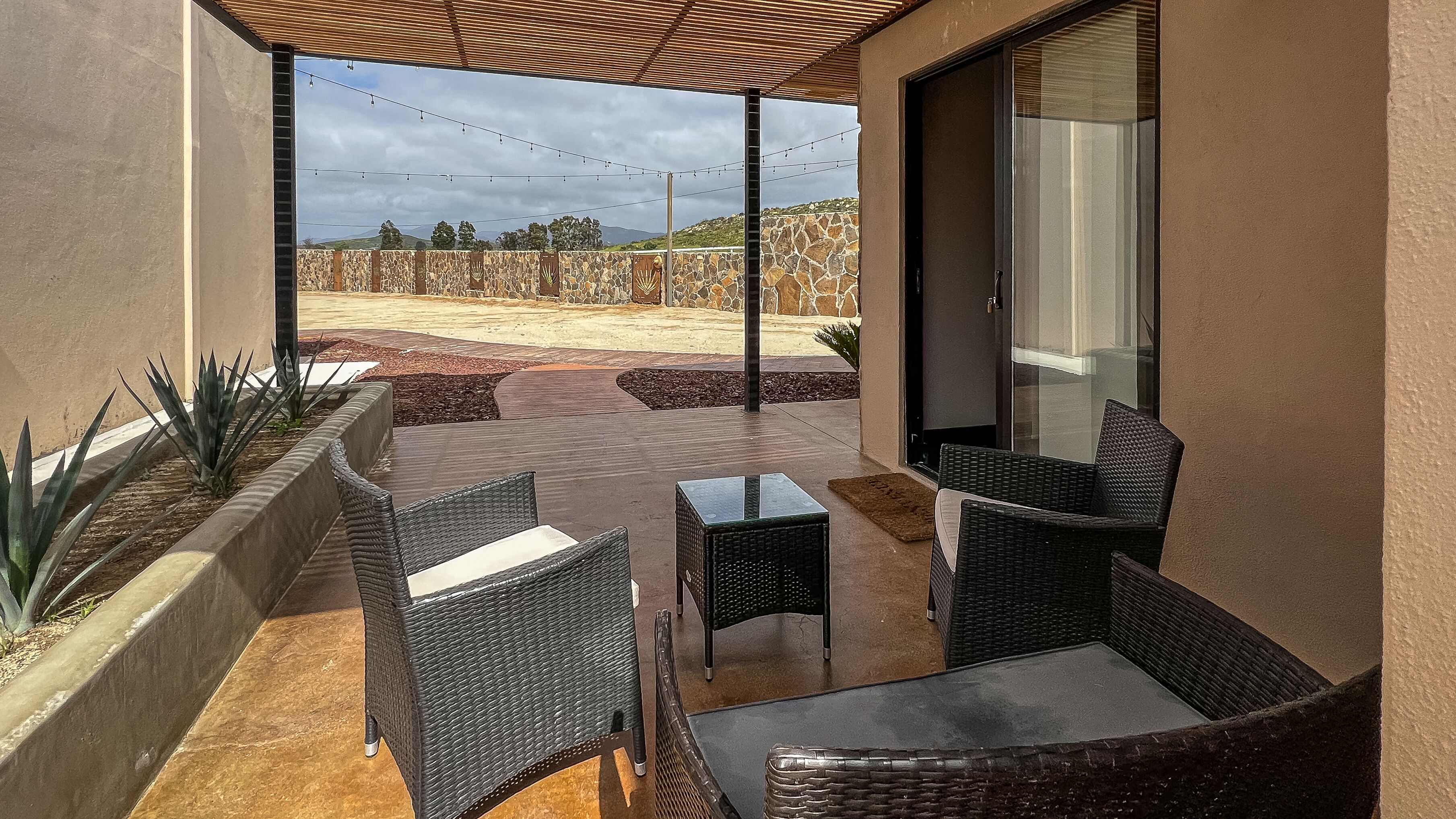An outdoor patio with wicker furniture, a stone wall, and a view of a hilly landscape.