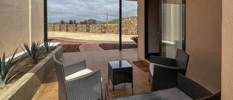 An outdoor patio with wicker furniture, a stone wall, and a view of a hilly landscape.